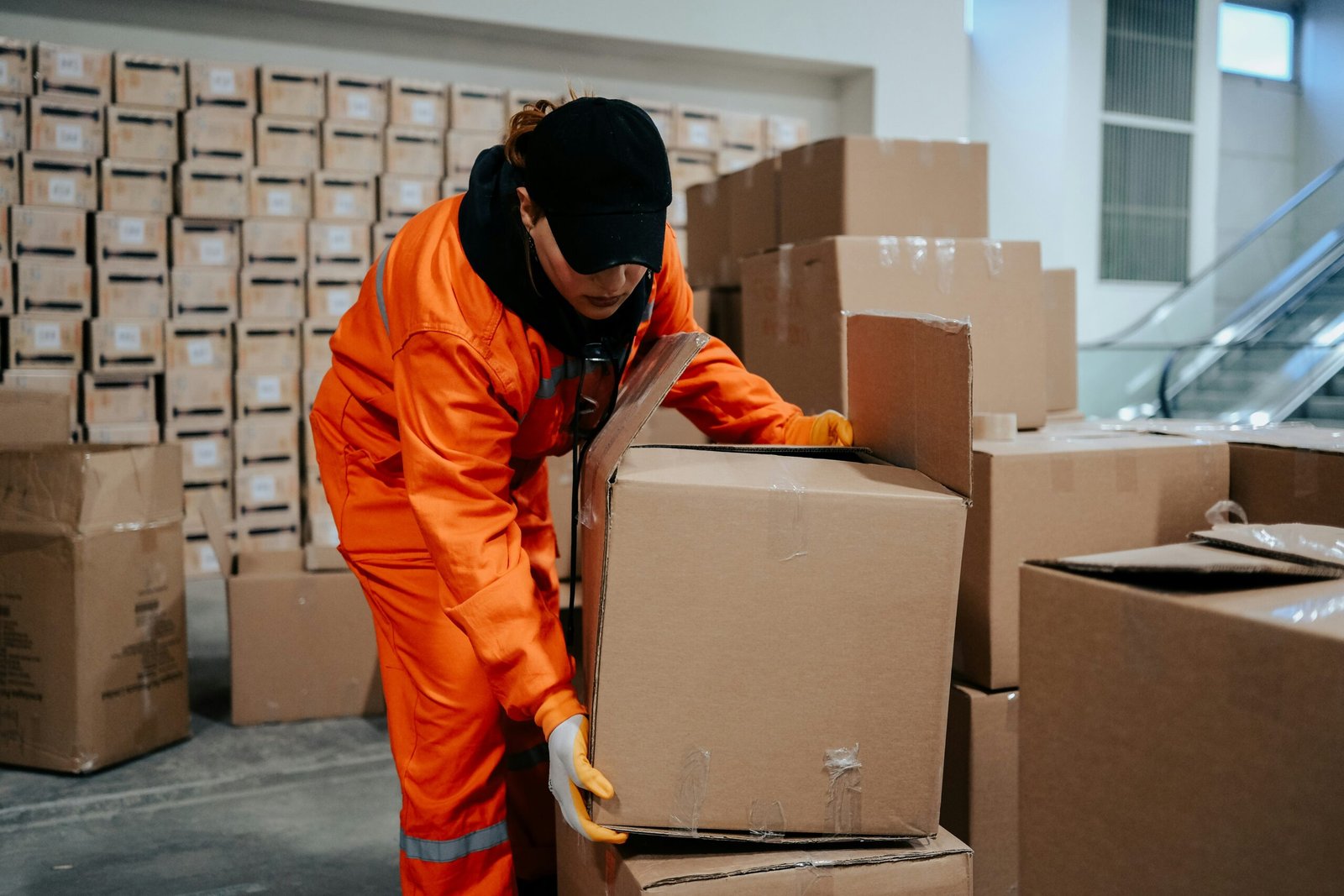 A man unpacking boxes he is in an orange jumpsuit and black baseball cap