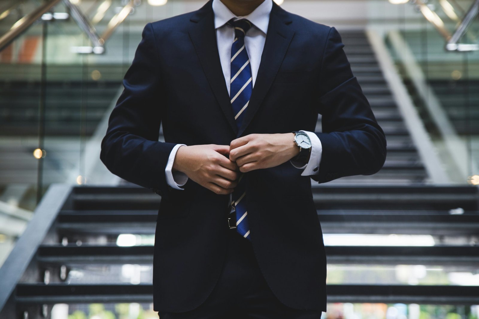 A man buttoning the middle button of his business suit, you cannot see his face